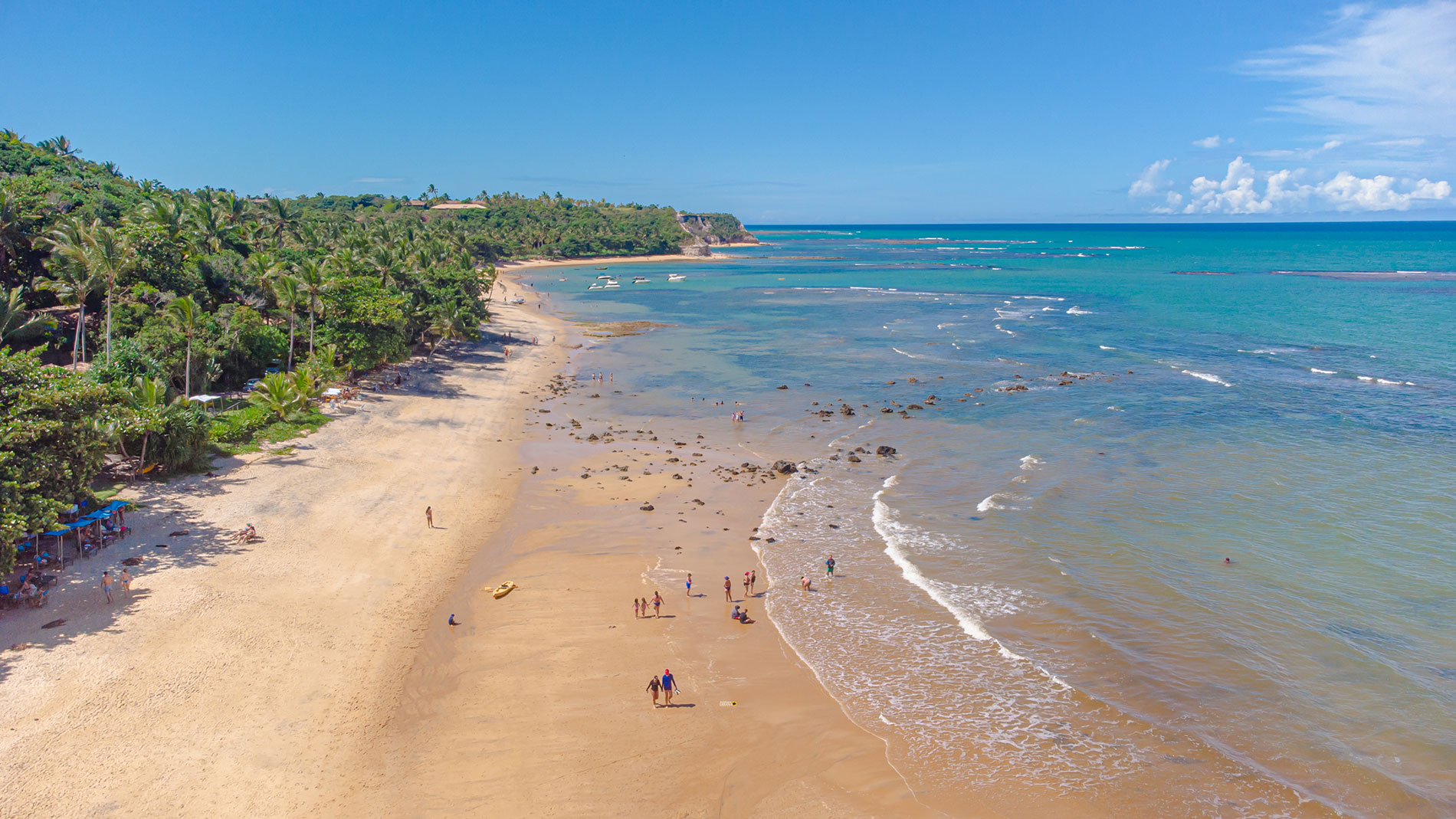 Vista aérea de trecho de mar calmo com recifes na Praia do Espelho e pessoas na água