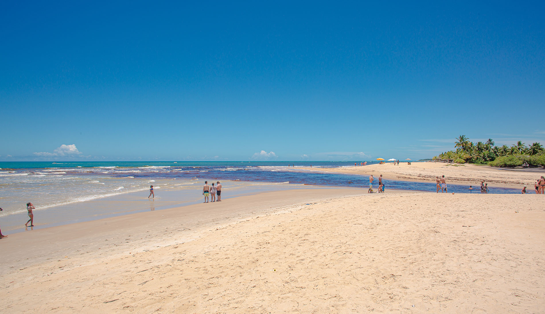 Praia de Trancoso com banhistas na areia e a foz de um rio encontrando o oceano